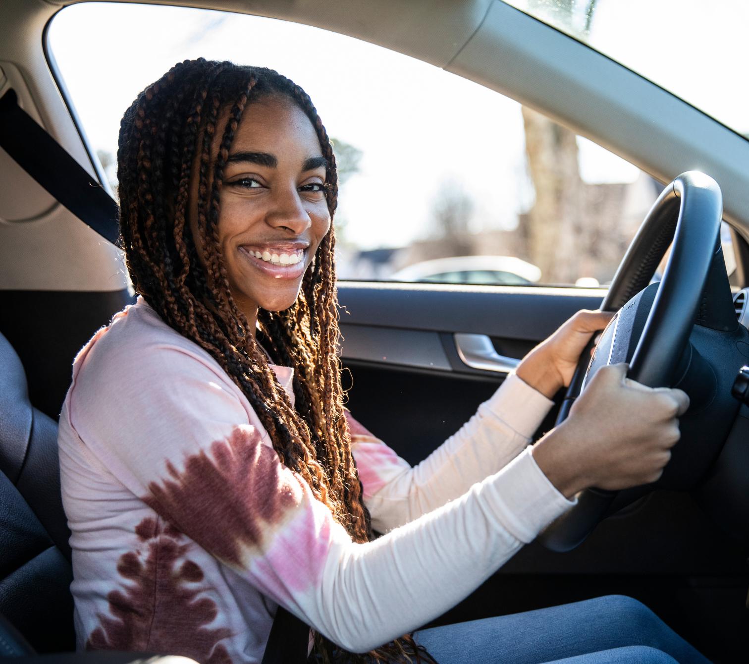 A teenager sits behind a car wheel, smiling.