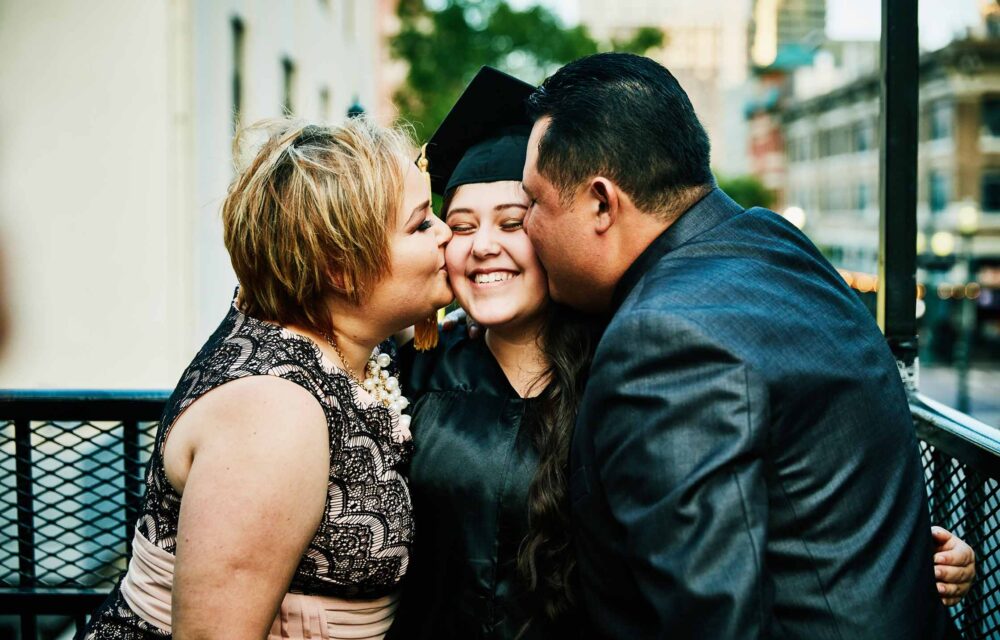 Mother and father kissing graduating daughter during family celebration