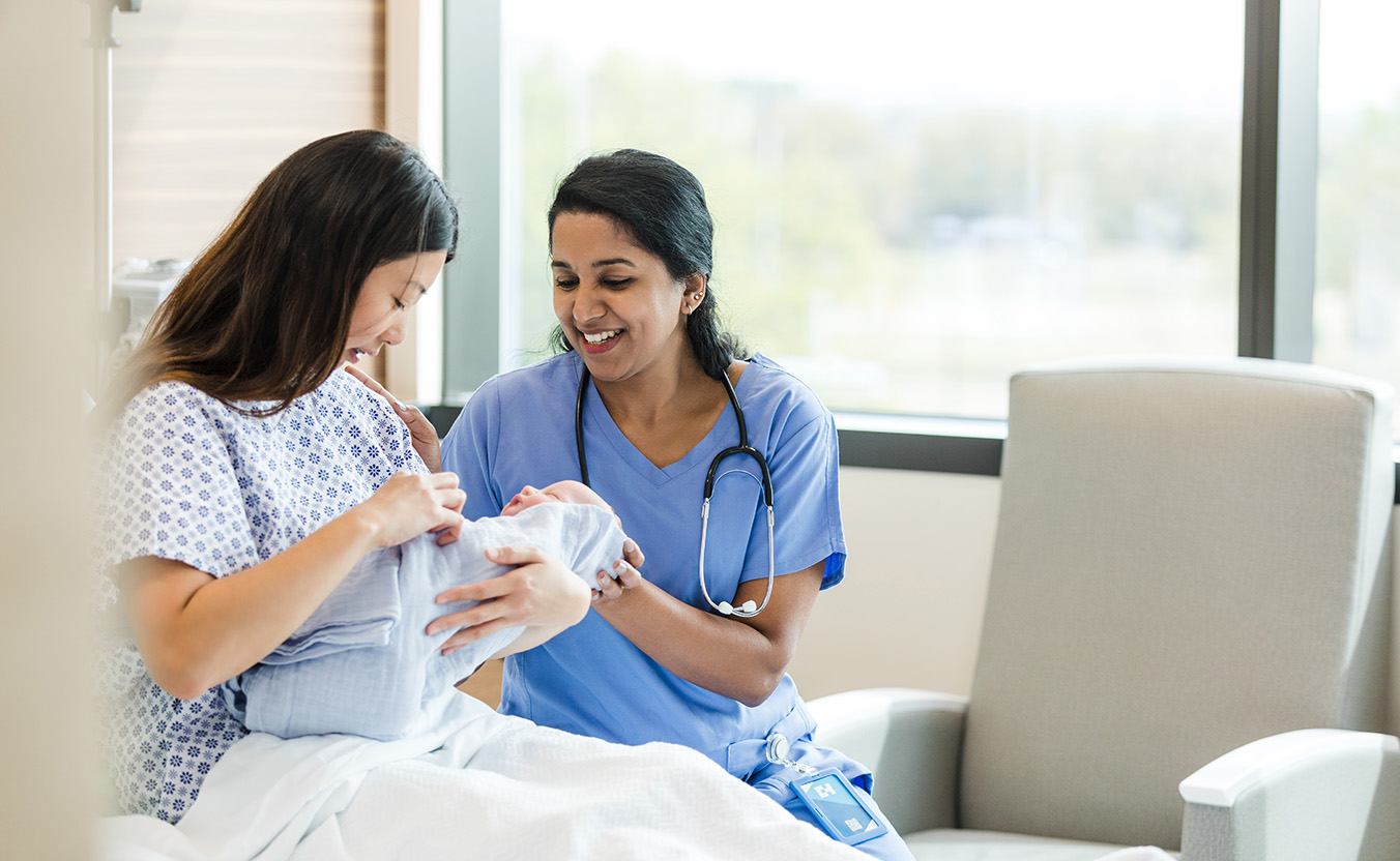 The female doctor sits bedside with the new mother to answer her questions about her newborn baby.